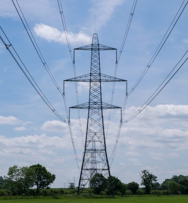A vertical shot of an overhead electric power transmission tower standing in a field under the blue sky