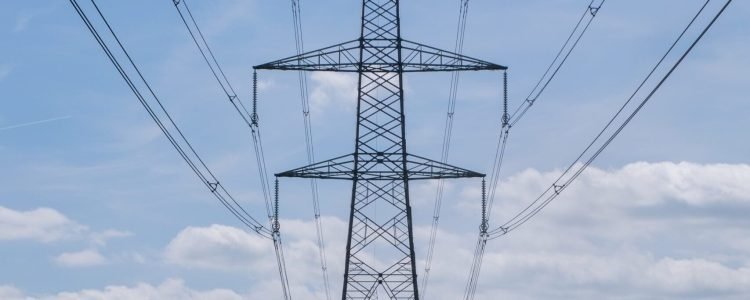 A vertical shot of an overhead electric power transmission tower standing in a field under the blue sky